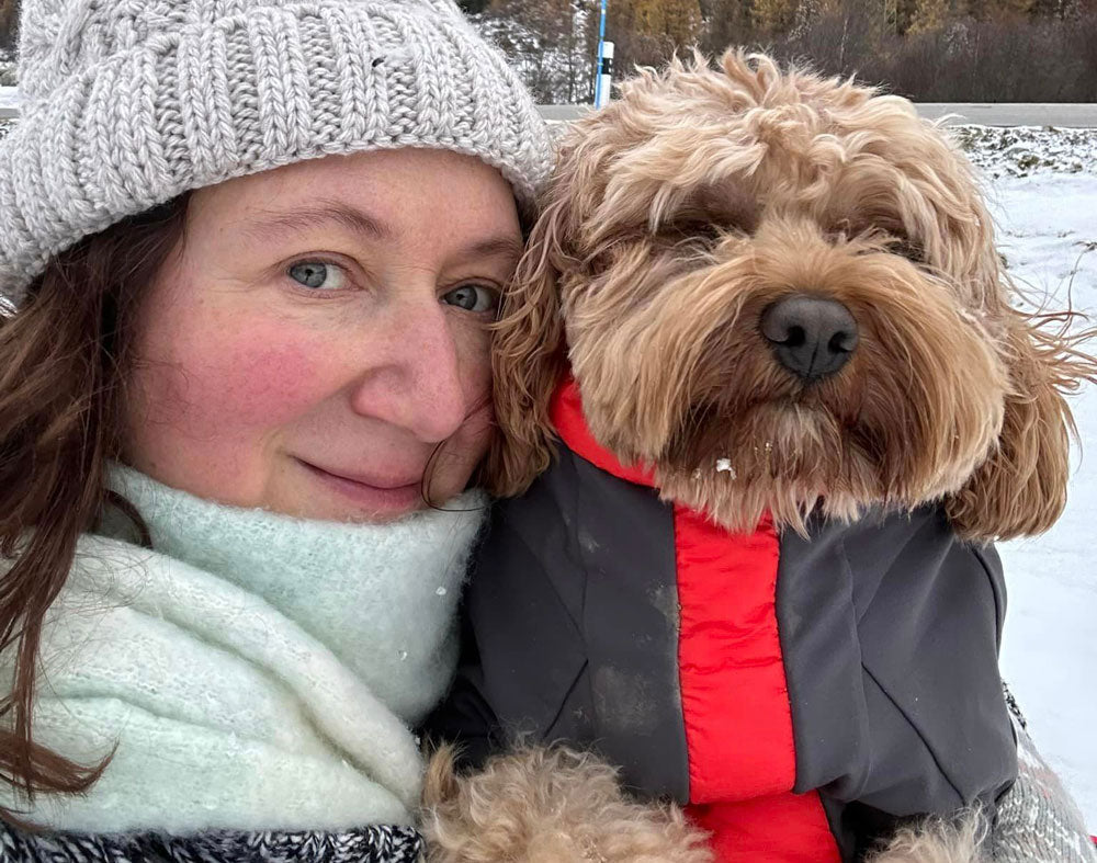 Woman in snow with dog in a coat, both wrapped up warm